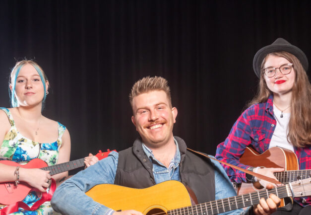 A photo of Sage Kelly with her ukulele, Jon Collins with his guitar, and Miranda Eno with her guitar on stage at Cardinia Cultural Centre.