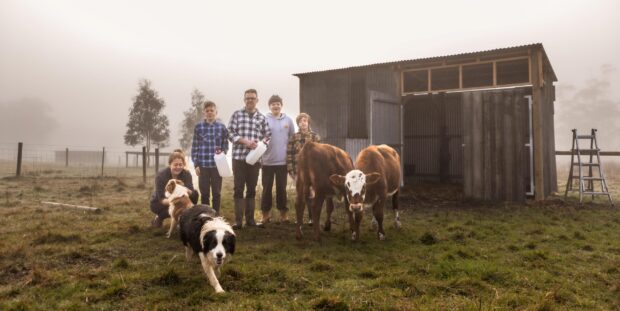 Photograph of a family of five posed in a foggy setting, with a shed, cows and dogs.