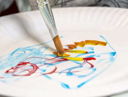 Photograph of child using a brush to make painted swirls on a paper plate.